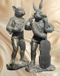 Par de esculturas em bronze representando um coelho e um gato músicos.